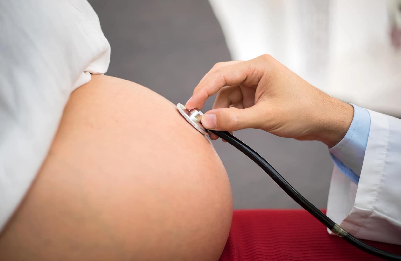 A gynecologist using a stethoscope to check a pregnant woman’s belly — addressing Common Myths About Visiting a Gynecologist.